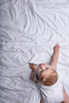 Curious cute infant baby boy crawling on a white bed craning his head back to look up at the camera in an overhead view with copy space