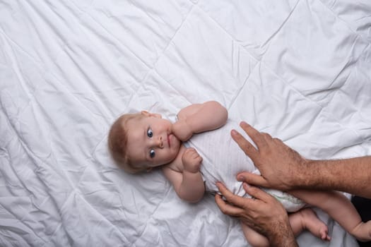 Father gently handling his son on a bed in a loving gesture placing his hands on the baby as it rests on its back viewed from overhead