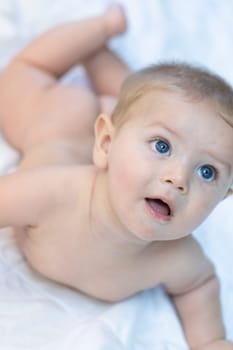 Innocent little baby staring up watching something off to the side with large trusting blue eyes as it lies naked on a bed