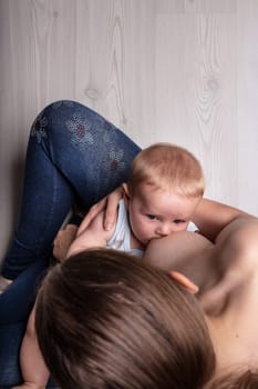 Young blond baby suckling on its mother in a view from the top of her head of the infant sucking on her teat and her bare breast, copy space on a neutral grey wood floor