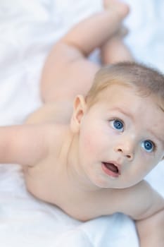 Curious calm little baby with large blue eyes raising itself up in its cot to look at something off to the side with a mesmerised expression
