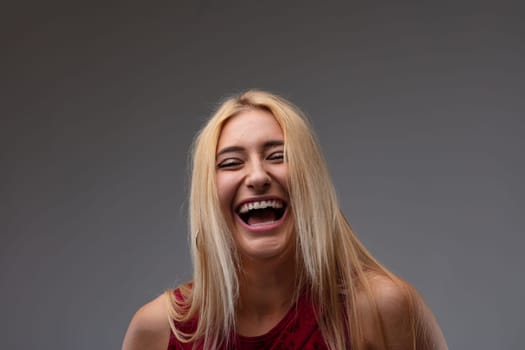 Carefree vivacious blond woman laughing at the camera enjoying a good joke in a close up portrait on a grey studio background