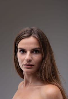 Intense beautiful young woman turning to stare at the camera with large wide open brown eyes and parted lips on a grey studio background