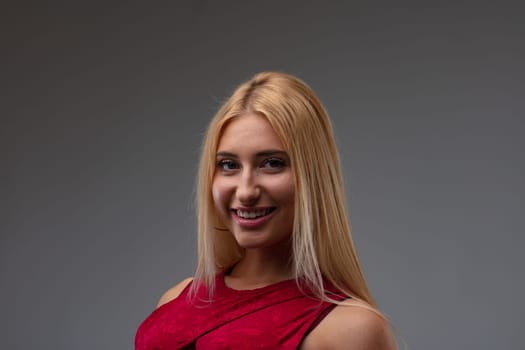 Stylish young blond woman with a vivacious beaming smile posing in a head and shoulders portrait against a grey studio background looking at the camera with copyspace