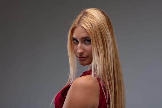 Seductive young woman with a sultry expression turning to look quietly at the camera over her shoulder in a head and shoulders portrait against a grey studio background with copyspace
