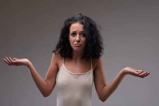 Confused young woman shrugging her shoulders with a frown of bewilderment as she gestures with her hands on a grey background