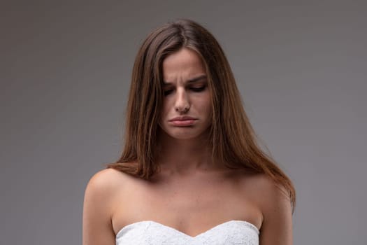 Sulky petulant attractive young woman scowling and pouting her lips in a close up head and shoulders portrait on a grey studio background