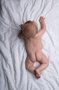 Tiny newborn baby attempting to crawl on white bedclothes viewed from above showing its cute little buttocks