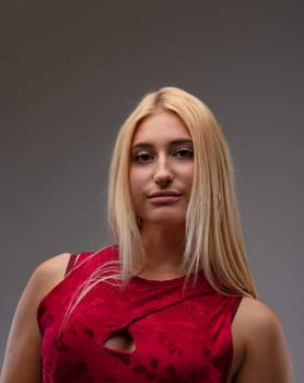 Elegant proud young blond woman in a stylish red top looking down at the camera with a thoughtful quiet smile against a grey studio background