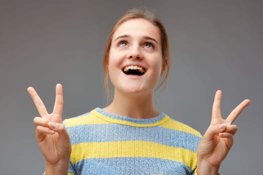 so lucky! young woman looks up to the sky, exclaiming for joy and making the V victory sign with both hands