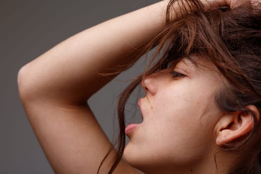 Sensual cropped portrait of a provocative young woman posing with mouth open and hand raised to her tousled long brown hair viewed in profile