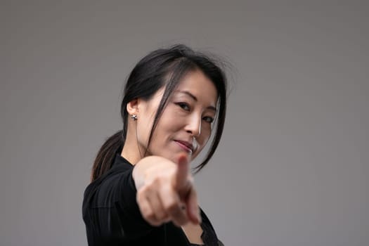 Woman pointing at the camera in blame or identification pr expressing a choice with a serious thoughtful expression over a grey studio background with copyspace