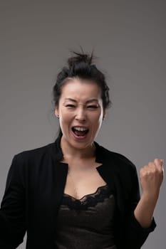 Enthusiastic motivated successful Asian business woman cheering and clenching her fist over a grey studio background with copyspace