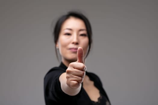 Successful motivated woman giving a thumbs up gesture with a quiet pleased smile of achievement over a grey studio background with copyspace