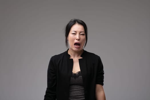 Woebegone Asian woman crying and wailing in her grief or bereavement over a grey studio background with copyspace
