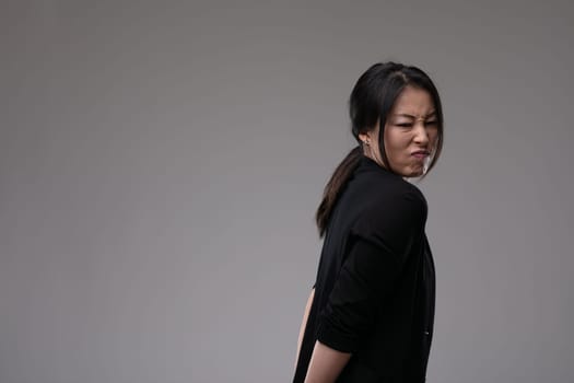 Disdainful Asian woman showing her disgust or dislike turning away with a grimace over a grey studio background with copyspace