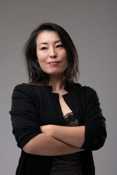 Confident professional Asian woman standing thinking with folded arms and a quiet pleased smile as she plans her strategy or enjoys her memories