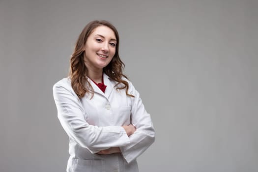 Confident friendly woman doctor or nurse in a lab coat standing with folded arms smiling at the camera on a grey background