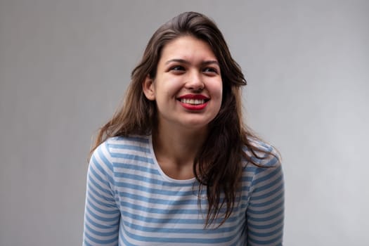 Positive young woman with a happy cheerful smile looking up to the side with a thoughtful expression over a grey studio background