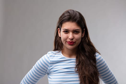 Amused attractive dark haired young woman grinning at the camera with laughing eyes over a grey studio background