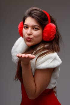 Sexy young woman in festive red outfit with matching ear muffs blowing a kiss at the camera in a Christmas, love and romance or holiday concept