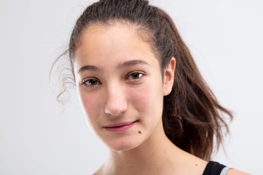 Attractive natural young woman with quiet smile and her long brunette hair in a ponytail looking pensively at the camera in close up on white