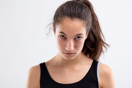 Sulky angry young woman glowering at the camera with a defiant expression and head lowered in a close up head and shoulders on white