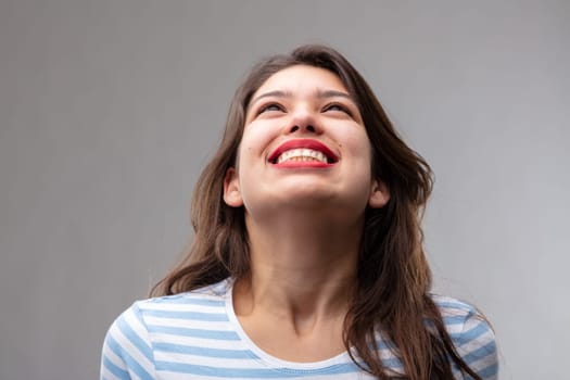 Happy carefree young woman with a joyful smile looking up smiling with pleasure and excitement over a grey studio background