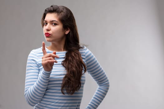 Argumentative young woman wagging her finger at the camera as she makes a point over a grey studio background with copy space