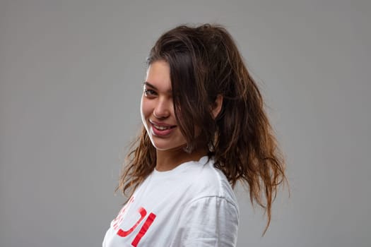 Cute attractive young woman with mussed up tousled long hair turning to look back at the camera with a lovely friendly smile in a close up studio portrait