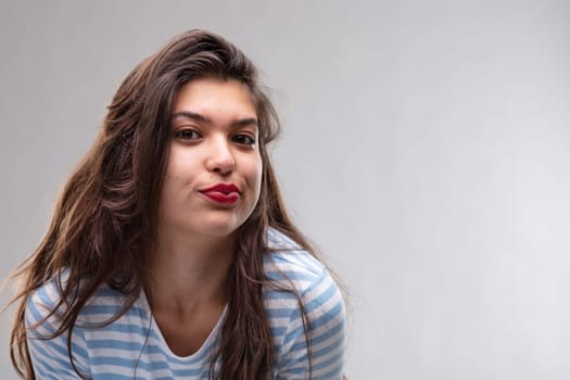 Young woman pulling a wry expression pursing her lips and looking sceptically at the camera in disbelief over a grey studio background