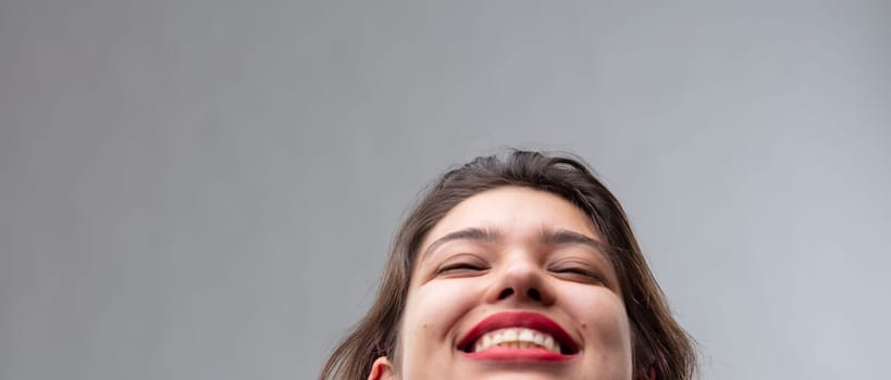 Panorama banner of a joyful young woman with her head thrown back and a beaming smile in a close up cropped portrait over a grey studio background with copy space