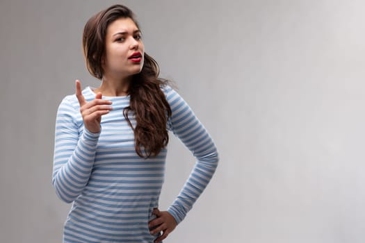 Young dogmatic woman having a serious discussion wagging her finger to make a point as she looks sideways at the camera over a grey studio background with copy space