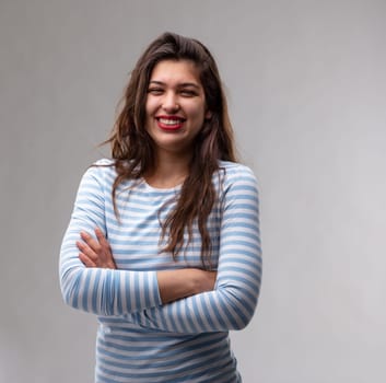 Happy self-assured young woman with folded arms standing looking at the camera with a vivacious warm friendly smile over a grey studio background