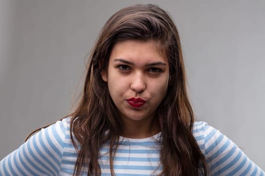Angry young woman pursing her lips and giving the camera a baleful glare with an intense expression over a grey studio background
