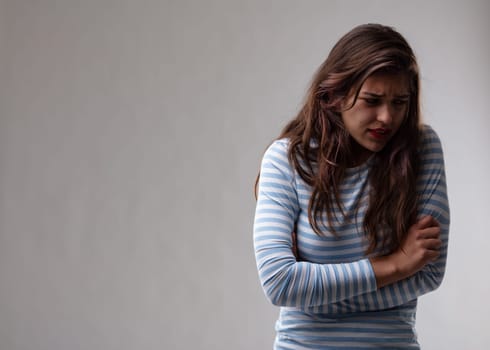 Young woman with a persecution complex reacting to rejection looking down with a troubled expression in a moody portrait over a grey studio background with copy space