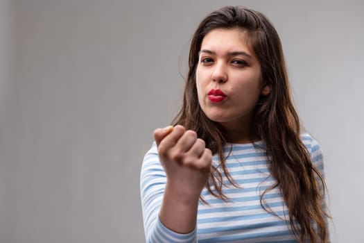 Menacing young woman brandishing her fist with a vengeful expression over a grey studio background