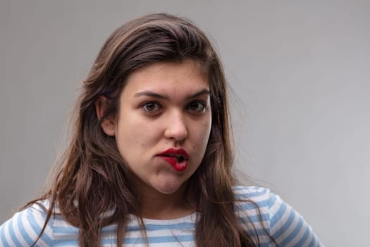 Undecided young woman with a moral dilemma biting her lower lip as she tries to reach a decision in a close up portrait over a grey studio background
