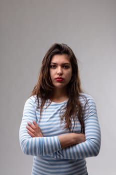 Serious young woman with an enigmatic expression staring earnestly at the camera with folded arms over a grey studio background