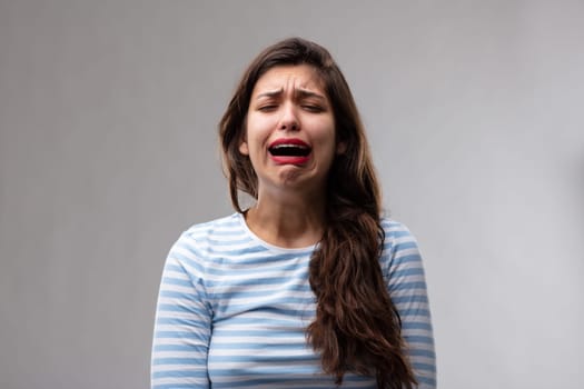 Emotional tearful young woman bawling in anguish expressing her feelings and emotions over a grey studio background