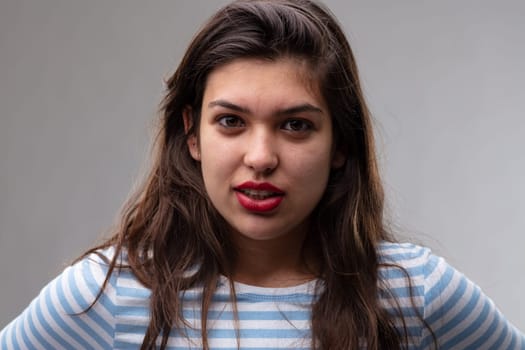Serious young woman with a penetrating stare looking directly into the camera with parted lips and a pensive expression over a grey studio background