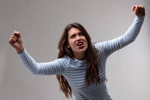 Victorious exultant young woman cheering and punching the air with her fists in a high angle view over a grey background
