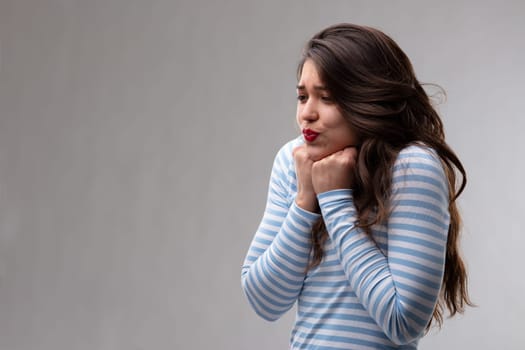 Young woman with a passionate crush or fancy holding her fists to the throat with pursing her lips over a grey background with copy space