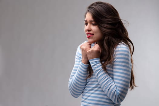 Young woman expressing a deep yearning or longing holding her fists to her chest with an agonised expression over a grey background with copy space