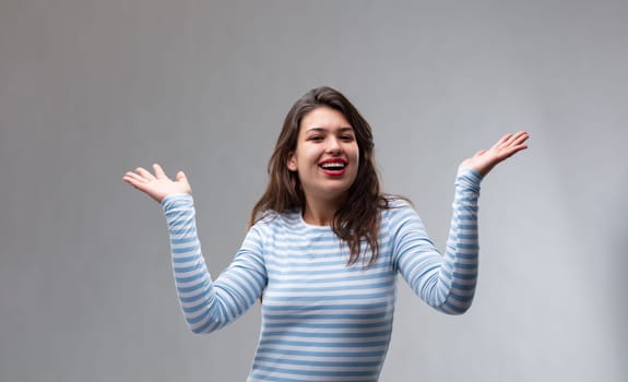 Happy joyful young woman gesturing with her hands and laughing over a grey studio background