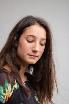 Thoughtful despondent young woman with a downcast expression in a close up head and shoulders portrait on grey