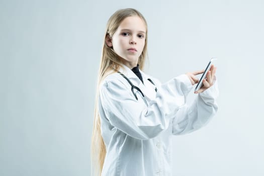 Serious young girl dressed up as a doctor or nurse holding a mobile phone in her hands as she turns to stare at the camera isolated on white