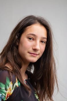Attractive young woman with a quiet smile and long brown hair turning to look thoughtfully at the camera over a grey background