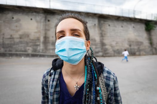 portrait of a young rebellious woman with rasta hairstyle in an urban setting wearing a protective mask covering her face and letting see her eyes facing adversity