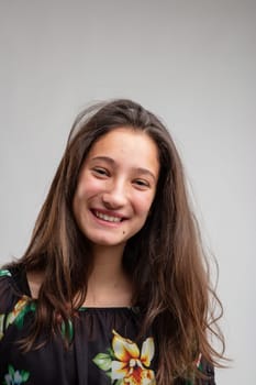 Happy friendly young woman with long straight tousled brunette hair smiling at the camera over a grey background in a close up portrait
